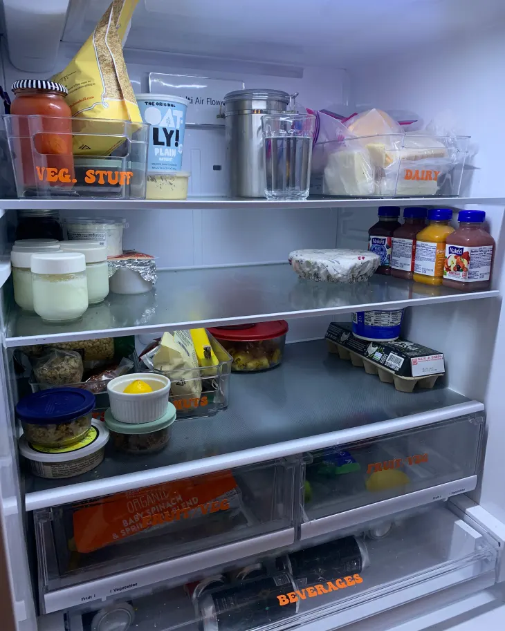 An open refrigerator, neatly organized and labeled with different food categories.